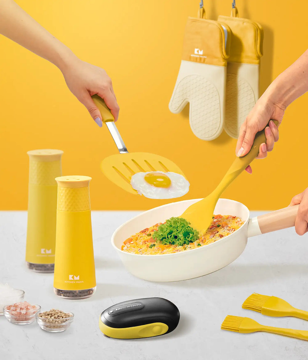 Kitchen Mama yellow kitchen tools, including can opener, spatulas, grinder, brushes, and oven mitts used while cooking a fried egg and pasta dish.