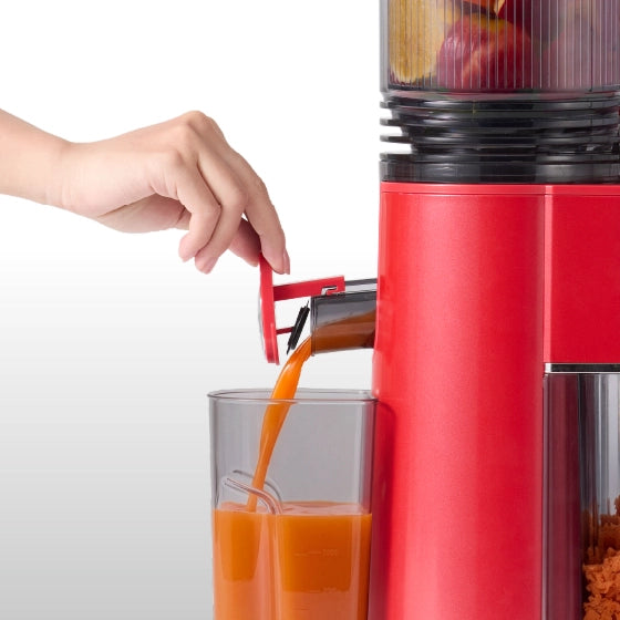 Fresh juice pouring from the Kitchen Mama EverVive cold press juicer into a juice container.