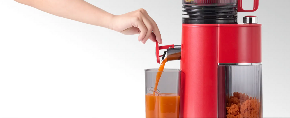Fresh juice pouring from the Kitchen Mama EverVive cold press juicer into a juice container.